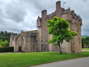 Image of Crathes Castle from the back, with a large green tree before it.