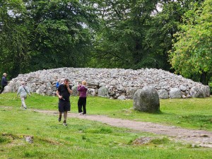 A large mound of stones at the Clava Cairns standing stones area. A couple of people walk in front.