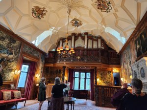 In a tall room with a decorated ceiling, there is a pipe organ with actual pipes near the roof