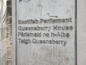 Sign in front of the Scottish Parliament that says Queesnberry House, Parlamaid na h'Albe Taigh Queensberry. (That second part is in Gaelic.)