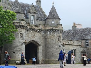 Image of the entrance to the outer courtyard of Holyrood Palace, with turrets and people walking