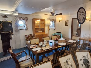 A small dining room with a captain's uniform behind glass hanging up behind it