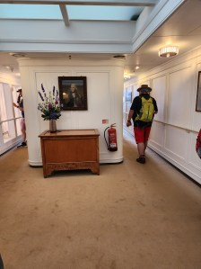 A boring hallway between staterooms on the ship. A man with a backpack is walking away from the camera.