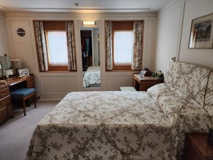 In the foreground a bed with an ugly green print bedstead In the background 2 large windows. This is Prince Philip's stateroom.