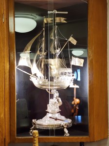 A silver statue of a ship, but it's behind glass so there's a lot of glare.