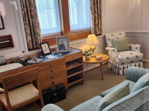 A room with a blue sofa and printed chair, as well as a desk; this is the Queen's office