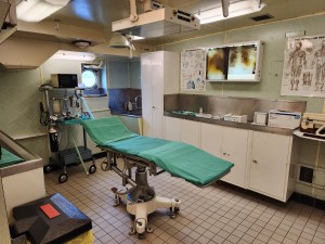 A green patient exam bed stands in the ship's surgery