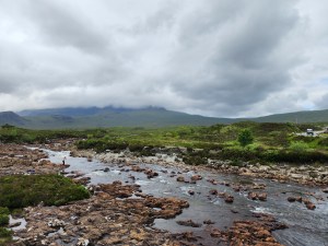 A landscape of a stream and mountains under a cloudy sky