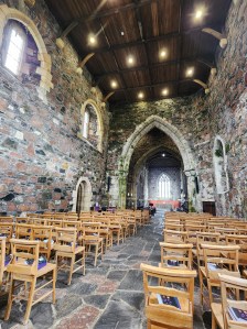 A long view of the inside of the church, featuring wooden chairs in the foreground an a large stone arch in the back.