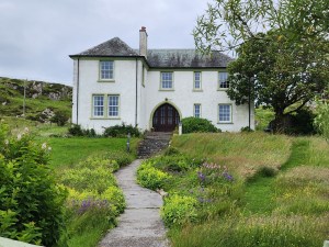 A big house with lush gardens in the foreground. It is George MacLeod's summer home, near the Abbey