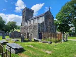 A tall, thin stone church next to some grave stones